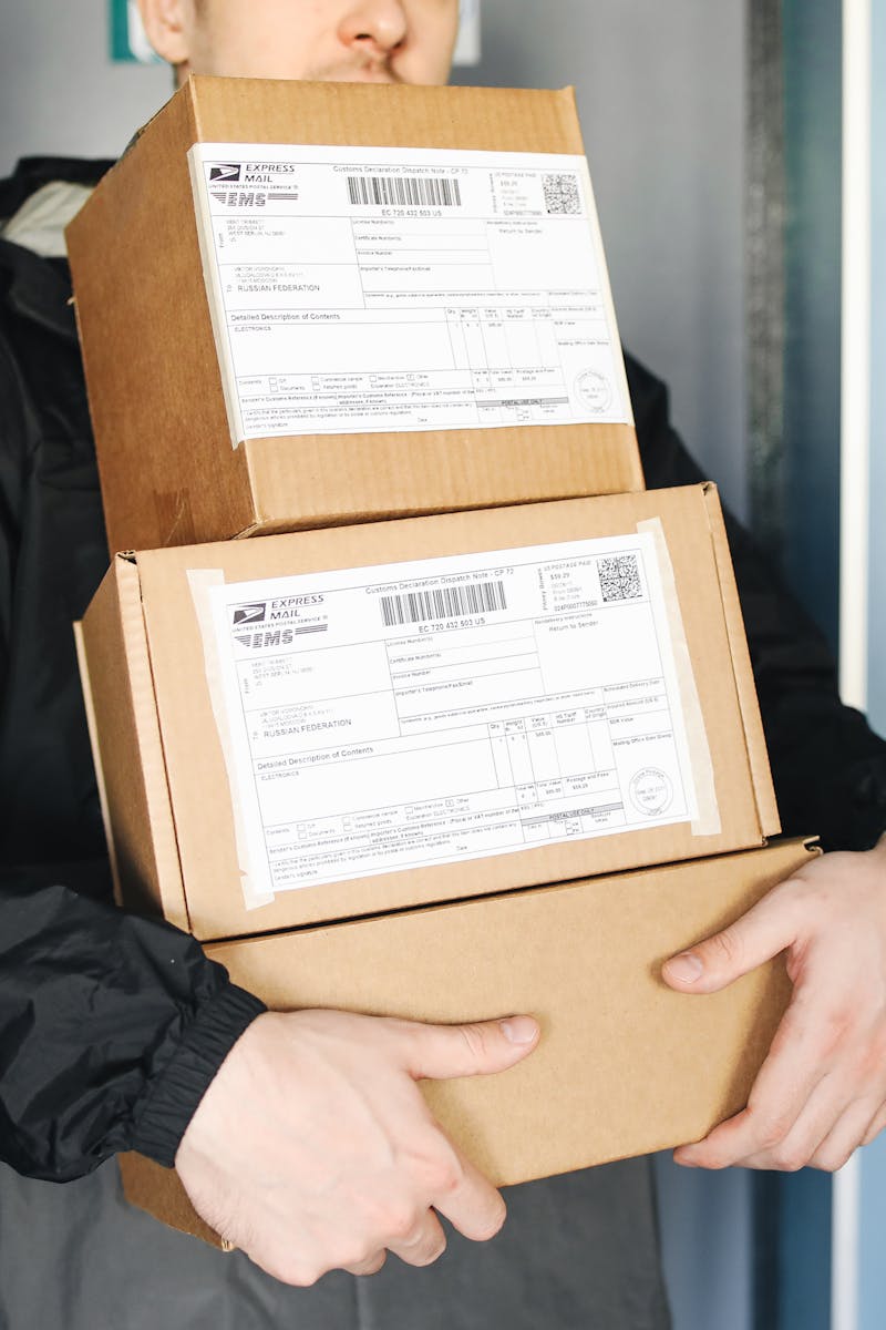 Courier carrying stacked cardboard packages for delivery service indoors.